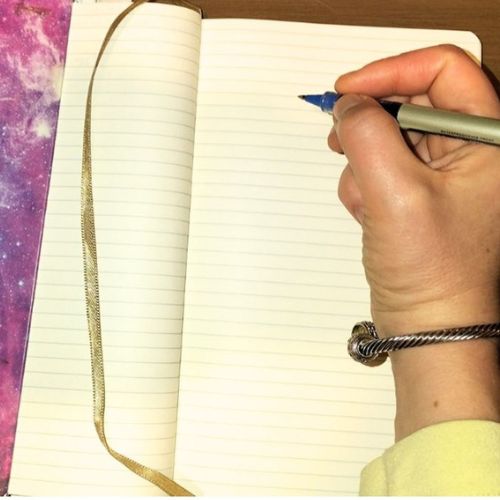 I am holding a pen, writing in a notebook.