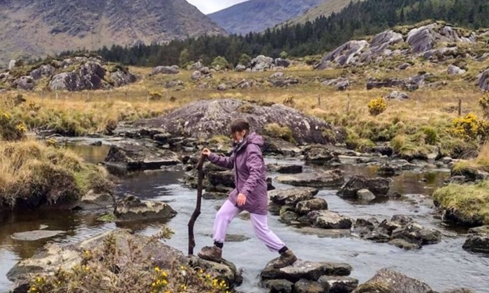 I am walking on stones to cross a river with mountains in the background.