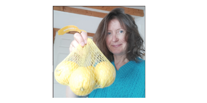 I am holding a bright yellow net filled with lemons. It has a plastic tag attached.