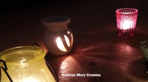 Candles in colourful glass holders. Pink, green, and yellow in a dark room.