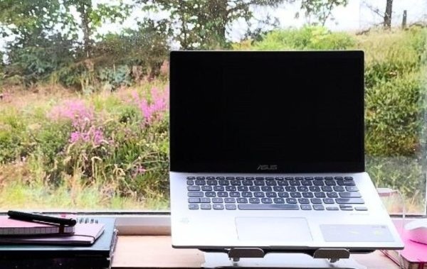 My laptop with a pile of notebooks. Heather and trees can be seen through the window.