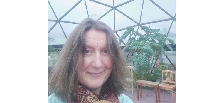 Photo of Kathryn Mary Crowley in a geodesic dome with plants. in the background are chairs and tables arranged for a workshop.